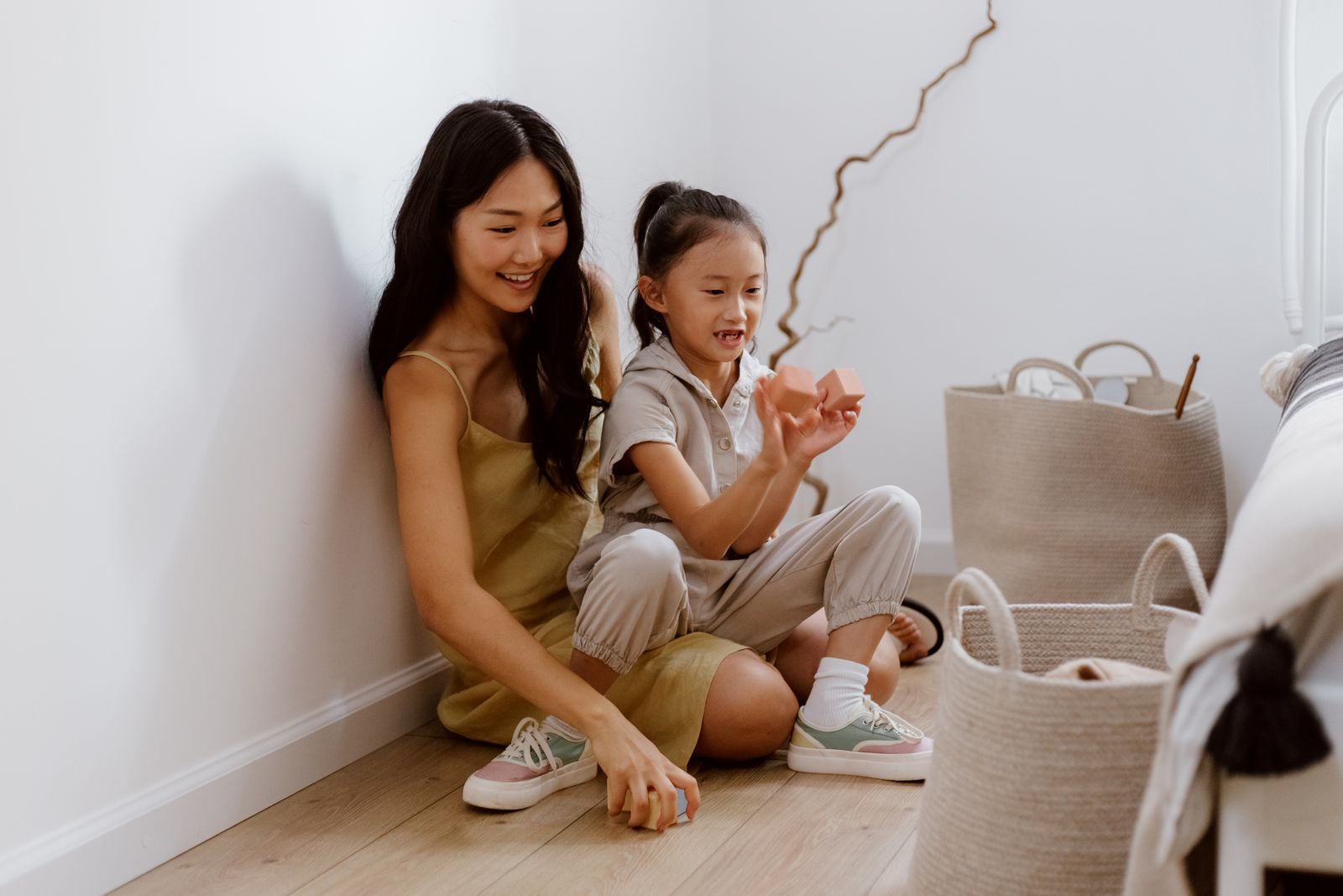 A mother and her young daughter sit on a living room floor, laughing as they play together